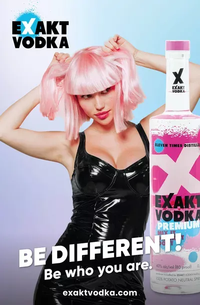 Eine Frau mit pinkfarbenen Haaren in einem schwarzen Lack-Kleid steht neben einer Flasche Wodka.