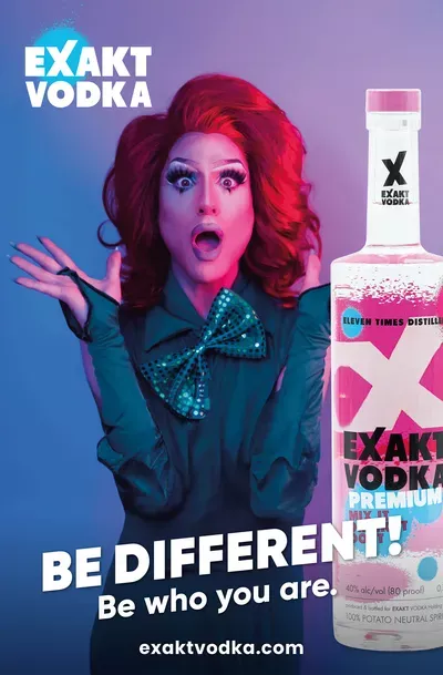 Eine Frau mit roten Haaren in einem grünen Kleid mit einer großen Fliege steht neben einer Vodka Flasche